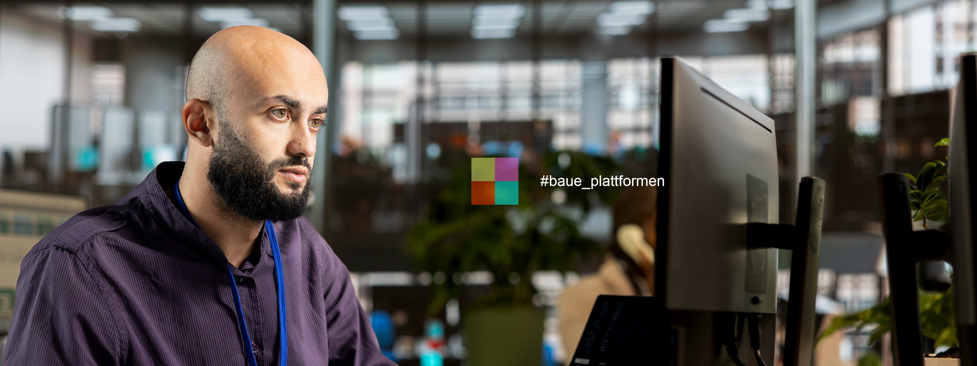 Junger Mann mit Bart und Glatze sitzt vor Bildschirm und programmiert